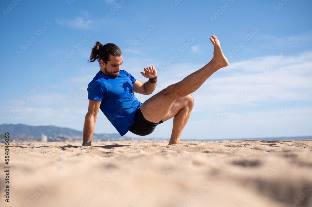 Young man with beard and ponytail performing exercises on the beach sand. Sports concept. Young man with beard and ponytail performing exercises on the beach sand. Sports concept.