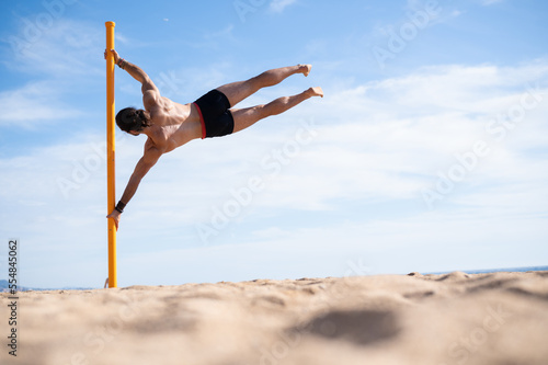 Young man doing the flag exercise on the beach. Calisthenics concept.