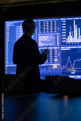 Back view of investor using charts and diagrams. Man working in dark office looking at digital screen with market data and analyzing information. Financial analytics, business activity concept
