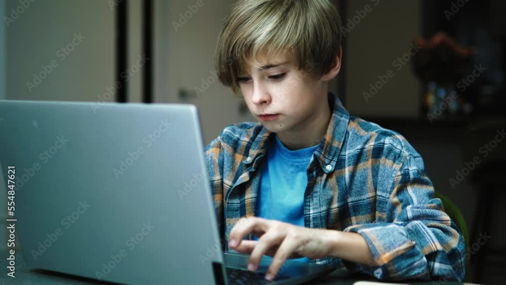 Cute handsome teenager boy using pc computer laptop for internet or doing homework, typing messages, chatting with friends, scrolling, browsing internet. Teenager addiction to gadgets Cute handsome teenager boy using pc computer laptop for internet or doing homework, typing messages, chatting with friends, scrolling, browsing internet. Teenager addiction to gadgets