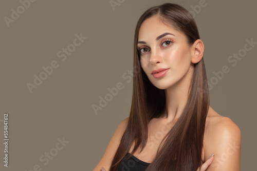 Portrait of a beautiful young brunette woman with long straight hair. On a gray background