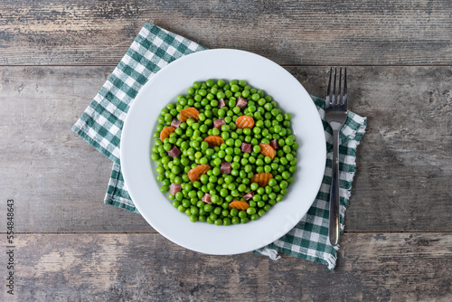 Green peas with serrano ham and carrot on wooden table. Top view