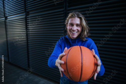 Portrait of young man with cap and sunglasses holding basketball ball,outdoor in city. Youth culture.