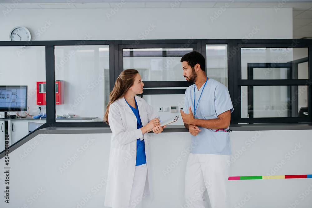 Young doctor talking at hospital reception with her colleague. Young doctor talking at hospital reception with her colleague.