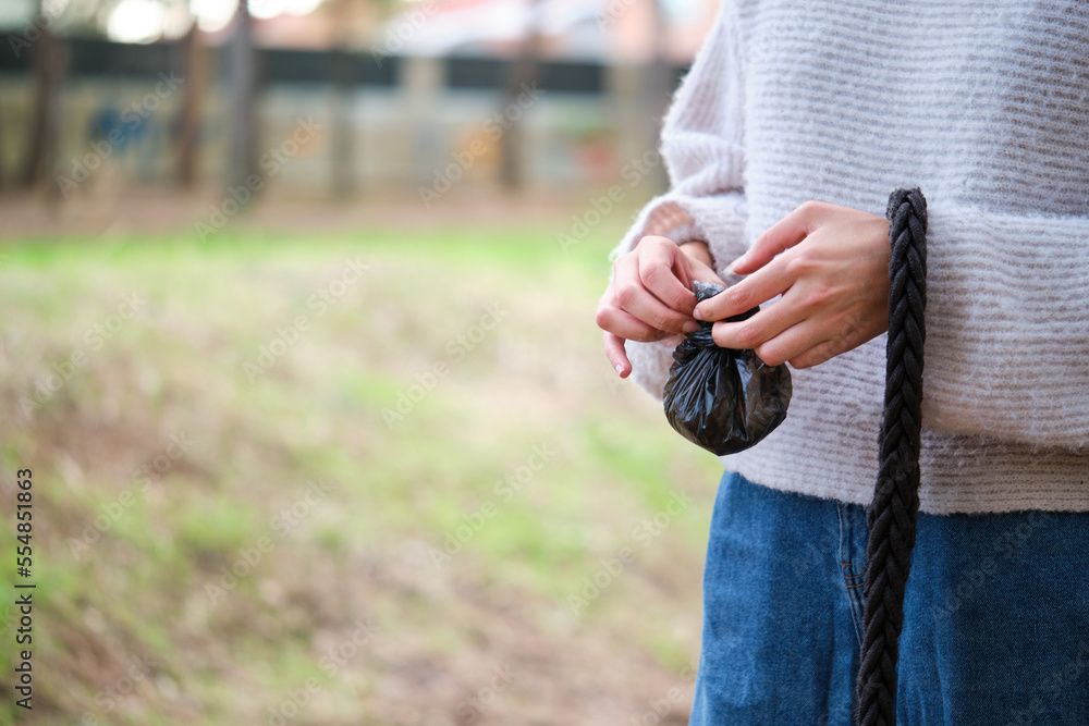 Cropped shot of young woman tying a knot in the dog trash bag after pet