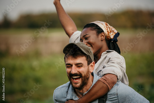 Playful, agriculture farmer couple having fun on a farm, countryside, or natura environment enjoying a rusti, sustainable living lifestyle. Happy, caring and in love husband giving wife piggyback ride © La Famiglia