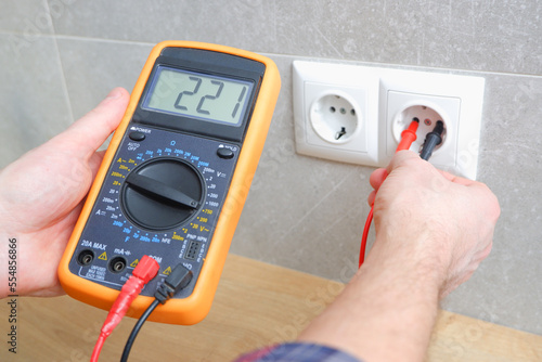 The electrician measures the voltage in the home network by inserting a voltmeter into the outlet. Close-up view of the hands with the appliance near the socket.