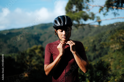 A young female cyclist is putting on her helmet to go for a bike ride.