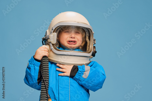 Portrait of little boy, child posing in astronaut costume over blue studio background. Feeling tired, crying © master1305