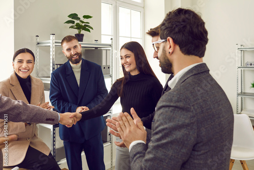 Young woman shakes hands with her colleagues while getting to know them in office. Friendly team of male and female employees welcome new team member. Concept of business relations and office team.
