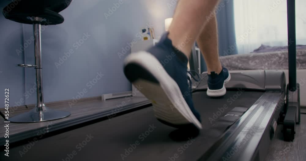 Closeup man feet running on running machine in home gym. Close up legs on treadmill Closeup man feet running on running machine in home gym. Close up legs on treadmill