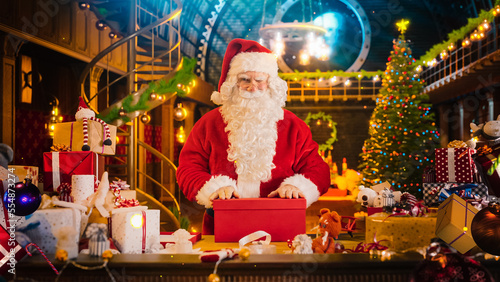 Santa Claus in Studio Workshop: Wrapping Christmas Gifts for all the Good Children to be Delivered on the Magical New Year Eve. He Packs the Teddy Bear As A Presents for an Excited Kid and Blinks