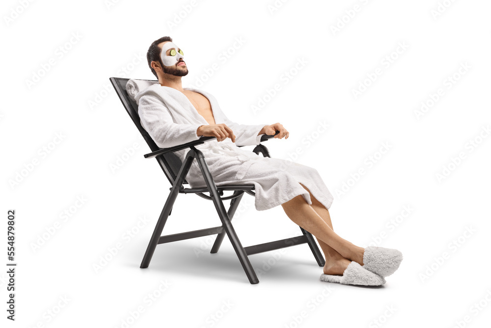 Man in a bathrobe with a face mask and cucumber on eyes sitting on a chair - obrazy, fototapety, plakaty 