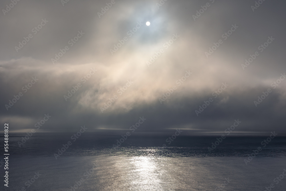 Fog clouds low above the calm water of the Irish Sea and the sun peaking through the clouds. 