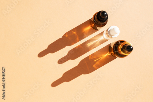 Glass bottles of cosmetic liquids, arranged in a row on the pastel beige surface, cast shadows. Flat style, copy space.