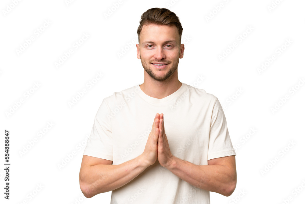 Young blonde caucasian man over isolated background keeps palm together. Person asks for something Young blonde caucasian man over isolated background keeps palm together. Person asks for something
