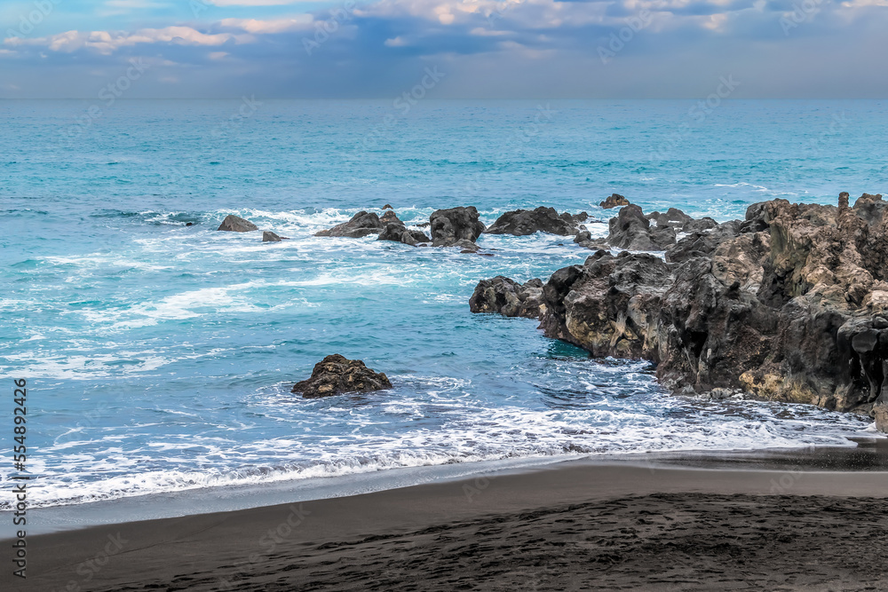 Stormy water during a hurricane on a black sand beach in the Canary Islands, Spain. Seascape of the Atlantic Ocean with rocks in blue sea among the waves with white foam and dramatic sky Stormy water during a hurricane on a black sand beach in the Canary Islands, Spain. Seascape of the Atlantic Ocean with rocks in blue sea among the waves with white foam and dramatic sky
