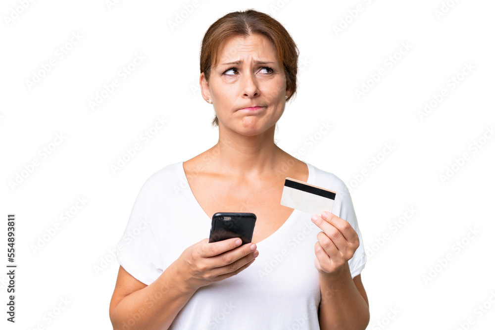 Middle-aged caucasian woman over isolated background buying with the mobile with a credit card while thinking Middle-aged caucasian woman over isolated background buying with the mobile with a credit card while thinking