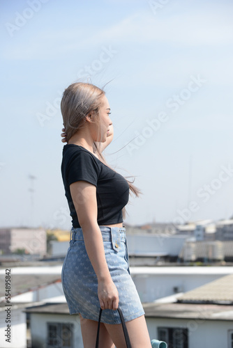 poortrait of caucasian beauty girl ashen hair wear black t shirt and jean skirt standing rroftop with small city view photo