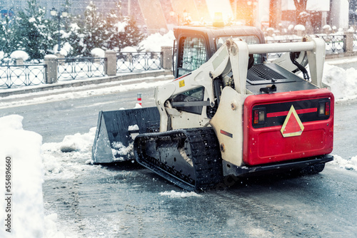 Mini tractor ski steer loader machine clean dirty snow of drive way. Cleaning city street, removing snow ice at heavy snowfalls and blizzard. Snowplow outdoors clean pavement sidewalk road driveway