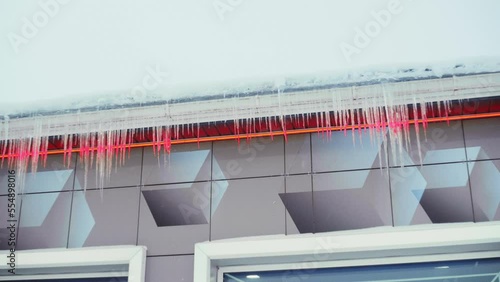 Large icicles hang from the overhang of the roof of the building. Falling ice- winter hazard for passersby photo