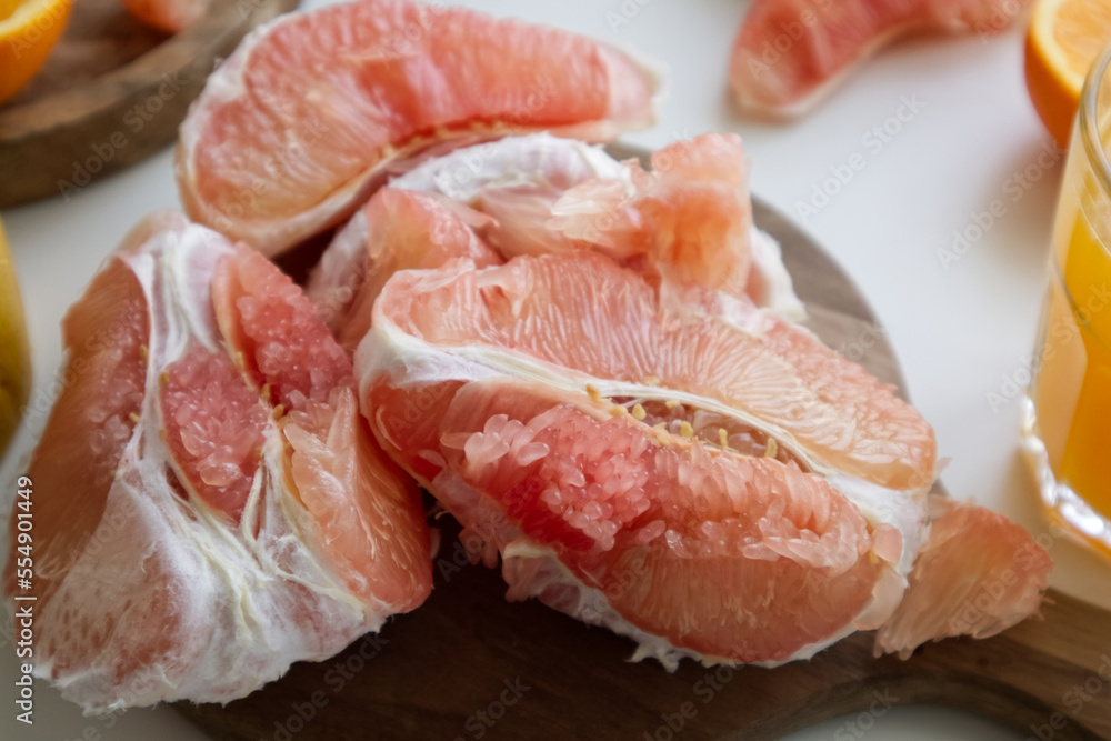Pomelo in a cut on a wooden stand near a glass of freshly squeezed juice and oranges Pomelo in a cut on a wooden stand near a glass of freshly squeezed juice and oranges