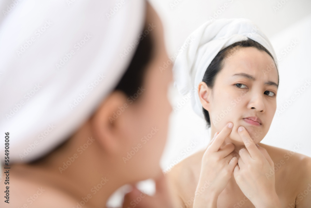 Problem skin. Concerned young asian women popping pimple on cheek while standing near mirror in bathroom. young asian women with acne Problem skin. Concerned young asian women popping pimple on cheek while standing near mirror in bathroom. young asian women with acne