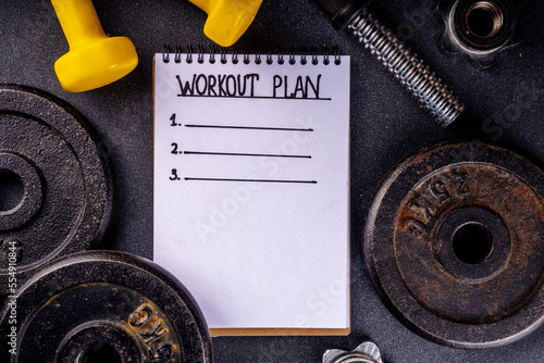 Fitness or bodybuilding background. Old hard iron dumbbells, small colorful dumbbells,  notepad with workout plan list. Back to gym concept, weight lifting sport flat lay top view copy space   photo