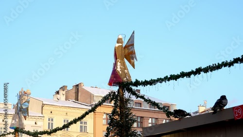 Christmas angel and doves on a snowy winter day against the blue sky, light installation of garlands in the form of an angel on the city square Main Market in Krakow. Polish Christmas Traditions