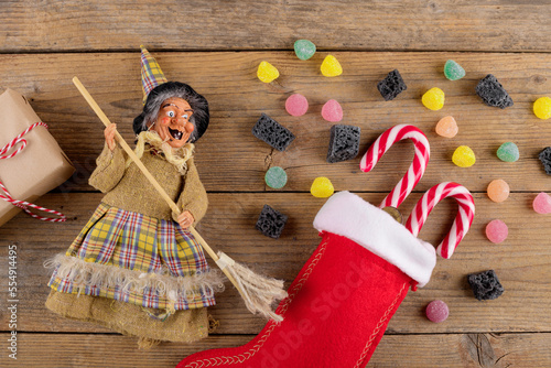 Quadro su tela The witch Befana and red stocking with sweet coal and candy on rustic wooden background