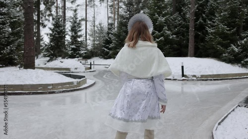 Snow Maiden figure skater, a cute young blonde in a white snow maiden costume with a kokoshnik , skating in the forest among snow-covered fir trees photo