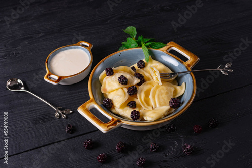 boiled dumplings sprinkled with blackberries and sour cream on a black background