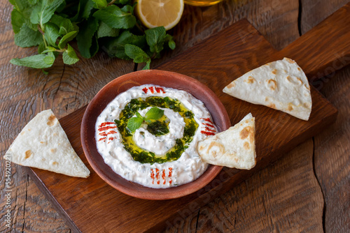 Turkish meze dish Haydari made from yogurt, cheese and fresh herbs. Dipping Sauce on a plate topped with a drizzle of olive oil and mint on top, with pita bread on the side for dipping. Horizontal photo
