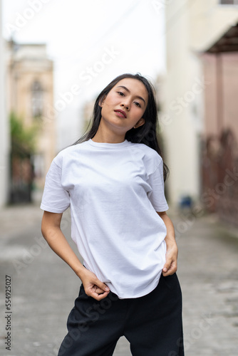 A young woman with a white blank shirt doing a cool pose with the with out of focus background