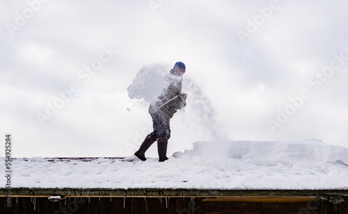 Man in action cleaning snow from the private house roof with shovel . Danger 