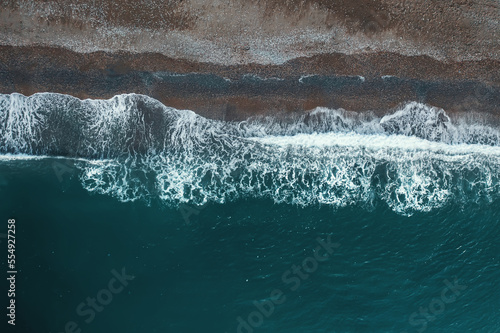 Aerial top view from drone of dark sand beach and sea or ocean water.
