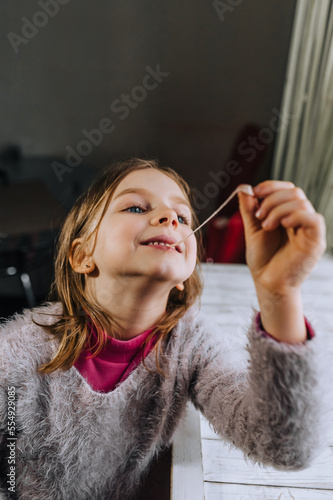 A beautiful smiling red-haired girl, a child chews a sweet chewing gum and stretches it with his hand. Photography, portrait.