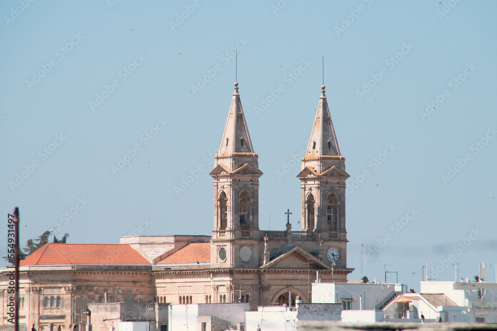 Campanarios de la Basílica santuario de San Cosme y Damián en Alberobello, Italia. Tejados y azoteas de los edificios que rodean el templo cristiano.