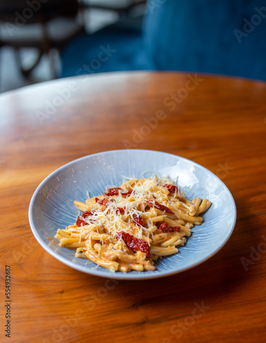 spicy pasta with cheese and red pepper in a blue plate on the table