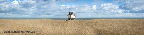 Wooden cabin boat tethered in the middle of the shingle beach at Dungeness along the Atlantic Coast; Dungeness, Kent, England, United Kingdom photo
