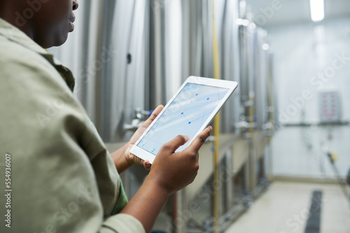 Brewery worker checking charts in application on tablet computer when controlling breer production