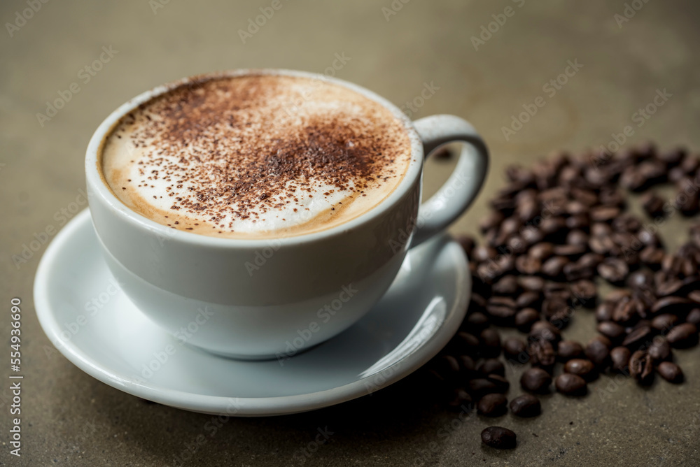 Cappuccino with foam and chocolate sprinkles and coffee beans on the counter beside the cup and saucer; Studio Cappuccino with foam and chocolate sprinkles and coffee beans on the counter beside the cup and saucer; Studio