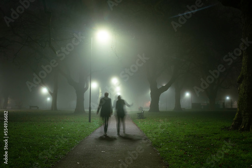 Motion blur and silhouette of two people walking on a foggy morning in London Fields, Shoreditch, London, UK; London, England