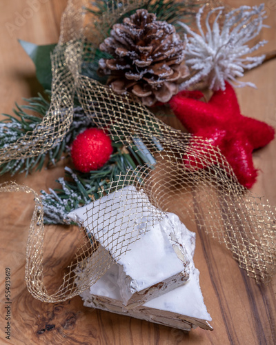 Two stacked pieces of white almond nougat with Christmas decorations on a wooden cutting board