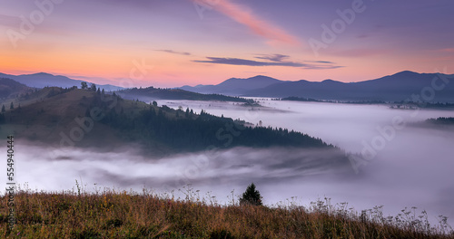 Incredible nature scenery im mountain. Beautiful natural landscape in the summer sunrise. Mountain valley with morning fog, colorful sky and visible silhouettes of Mountain ranges. Carpathian. Ukraine