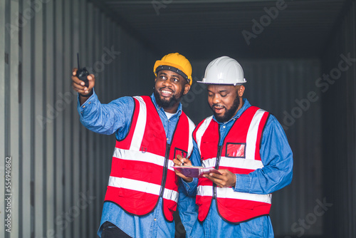 Portrait of Two African Engineer or foreman wears PPE checking container storage with cargo container background at sunset. Logistics global import or export shipping industrial concept.