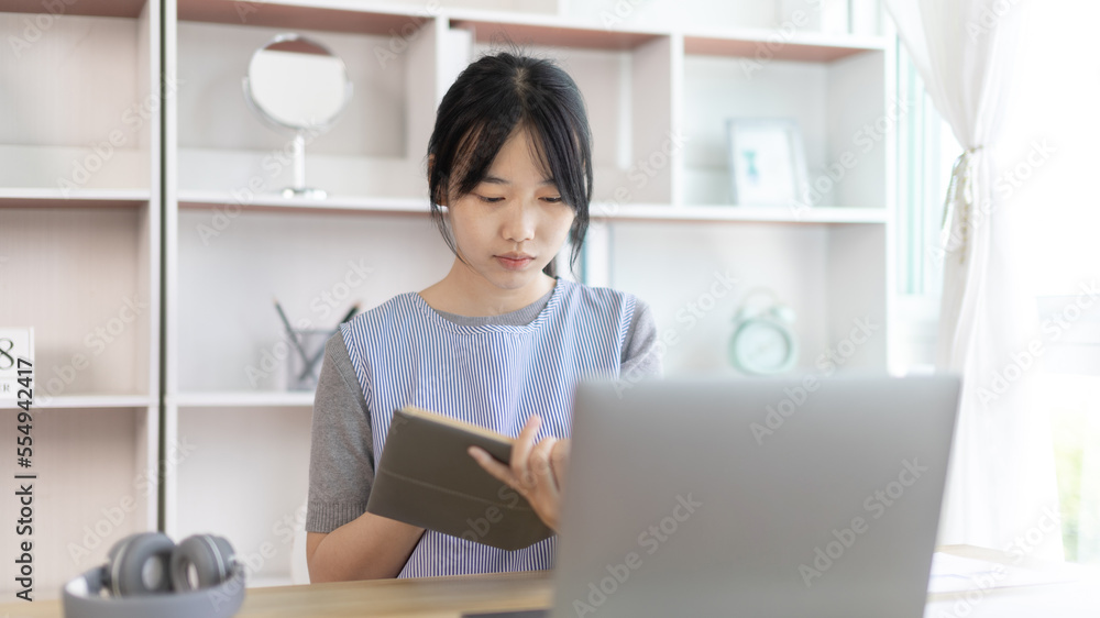 Asian woman taking notes in notebook while studying online in laptop at home, Video chat, Online communication , Stay home, New normal, Distance learning.., Social distancing, Learn online... Asian woman taking notes in notebook while studying online in laptop at home, Video chat, Online communication , Stay home, New normal, Distance learning.., Social distancing, Learn online...