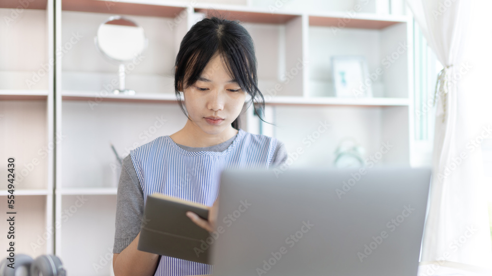 Asian woman taking notes in notebook while studying online in laptop at home, Video chat, Online communication , Stay home, New normal, Distance learning.., Social distancing, Learn online... Asian woman taking notes in notebook while studying online in laptop at home, Video chat, Online communication , Stay home, New normal, Distance learning.., Social distancing, Learn online...