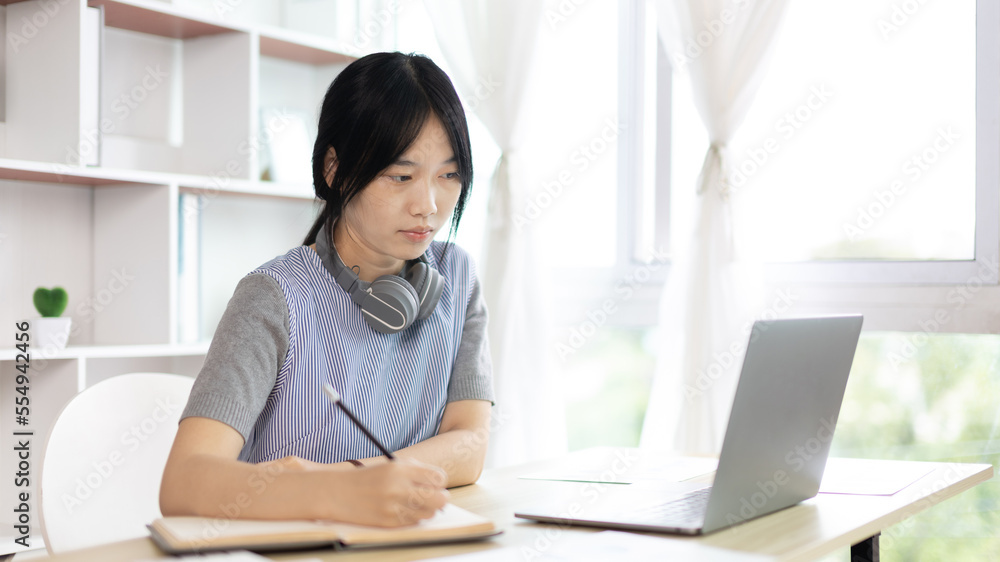 Asian woman taking notes in notebook while studying online in laptop at home, Video chat, Online communication , Stay home, New normal, Distance learning.., Social distancing, Learn online... Asian woman taking notes in notebook while studying online in laptop at home, Video chat, Online communication , Stay home, New normal, Distance learning.., Social distancing, Learn online...