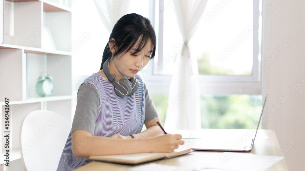 Asian woman taking notes in notebook while studying online in laptop at home, Video chat, Online communication , Stay home, New normal, Distance learning.., Social distancing, Learn online...
